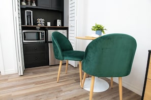 Una cocina moderna con microondas, tostadora y armarios. Hay dos sillas verdes con patas de madera.