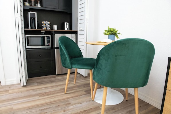 Cozinha moderna com micro-ondas, torradeira e armários. Há duas cadeiras verdes com pés de madeira.