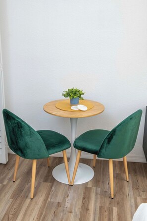 Mesa redonda com duas cadeiras de veludo verde, uma pequena planta e dois sabonetes brancos sobre a mesa.