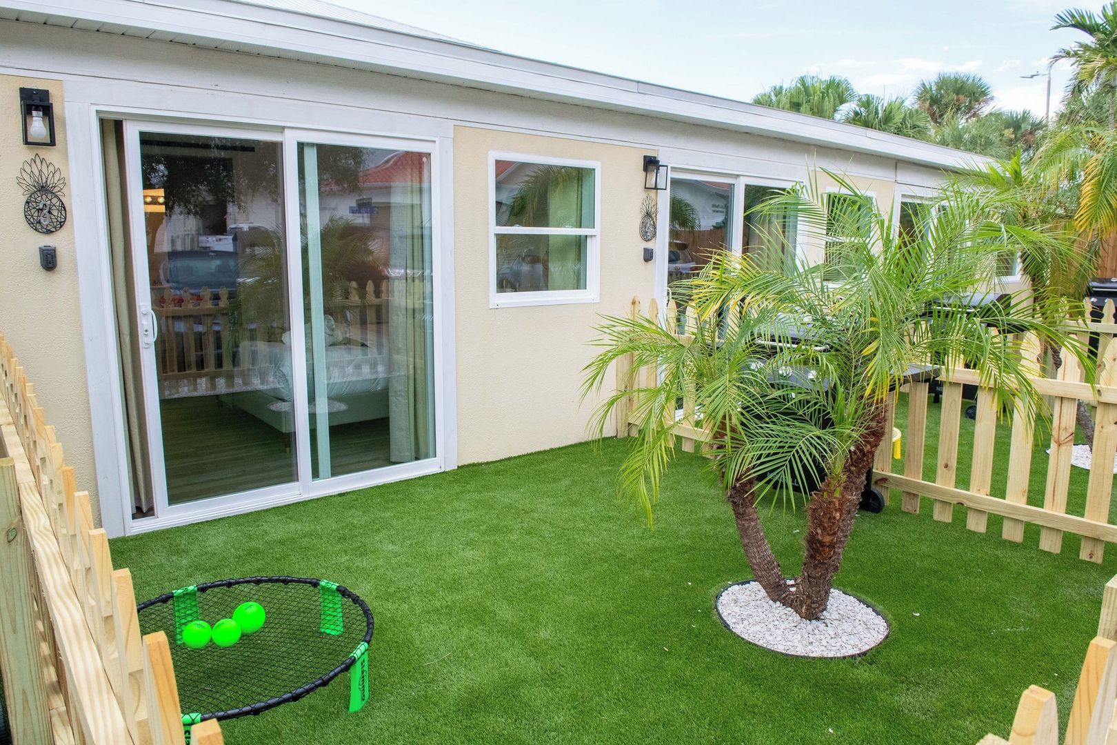 Propiedad residencial con patio, césped artificial, valla de madera y una palmera.