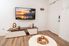 A modern living room with a flat-screen TV mounted on the wall, a wooden console table with storage, a round coffee table with a tray, and a white door.