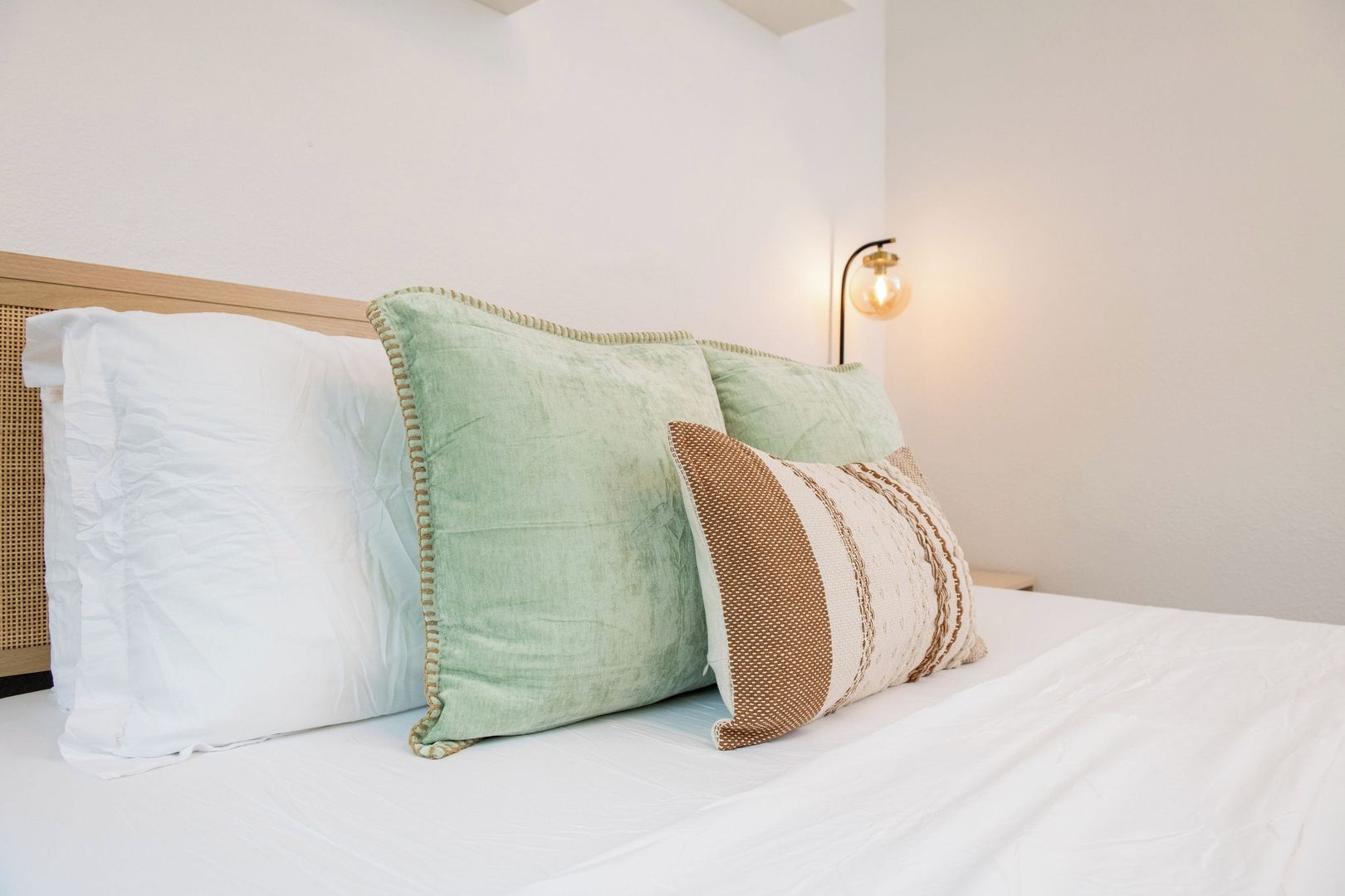 A bed with white bedding, a wooden headboard, and three pillows in different patterns.