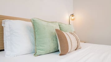 A bed with white bedding, a wooden headboard, and three pillows in different patterns.