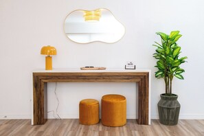 Une console en bois avec un miroir, deux tabourets, une lampe, une plante en pot et un petit panneau.