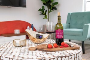 Une table ronde recouverte d’une nappe à motifs, une bouteille de vin, un verre et un bol rempli de fraises.