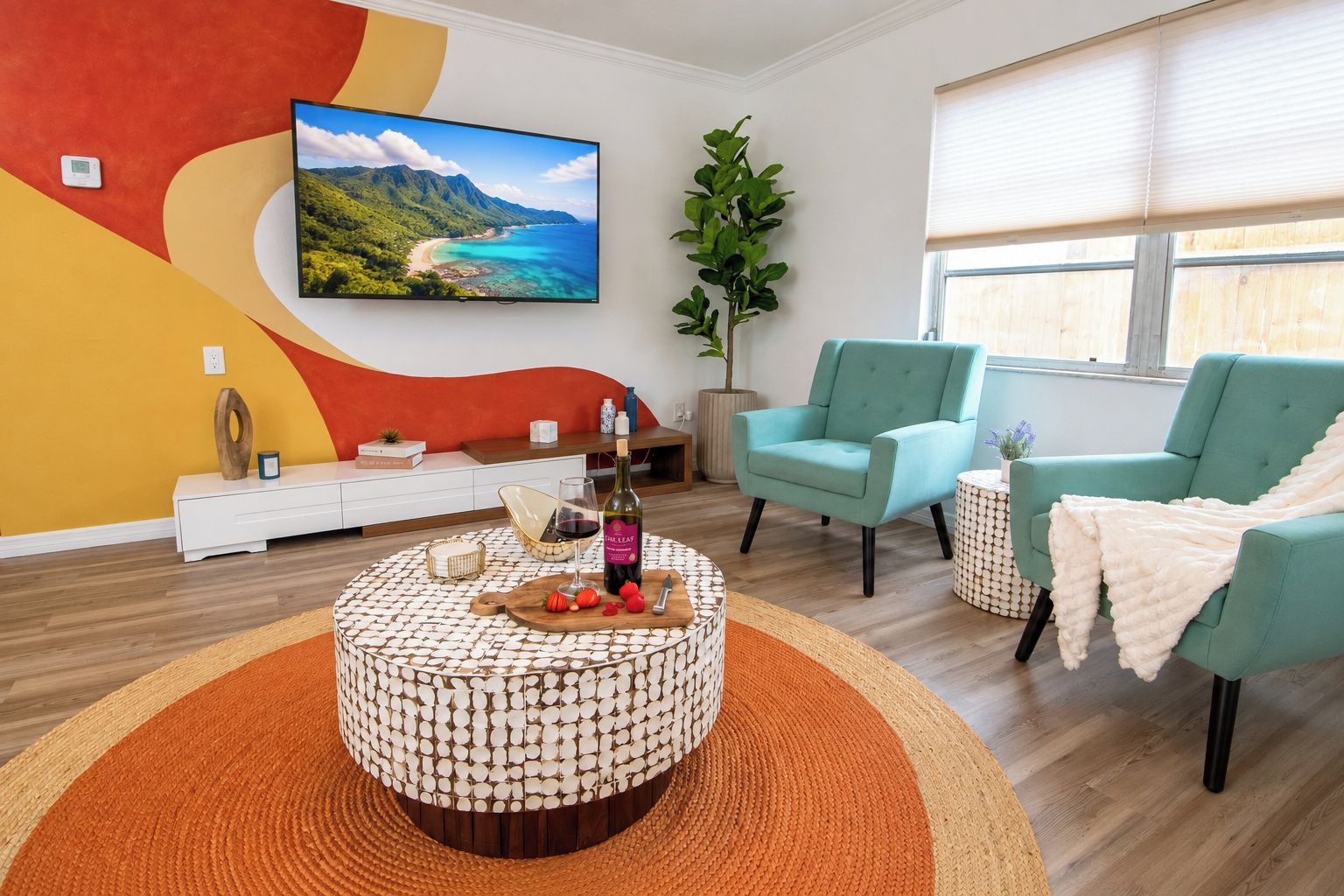 Una sala de estar moderna con una mesa redonda, dos sillones color turquesa, un televisor plano grande y una planta en maceta.