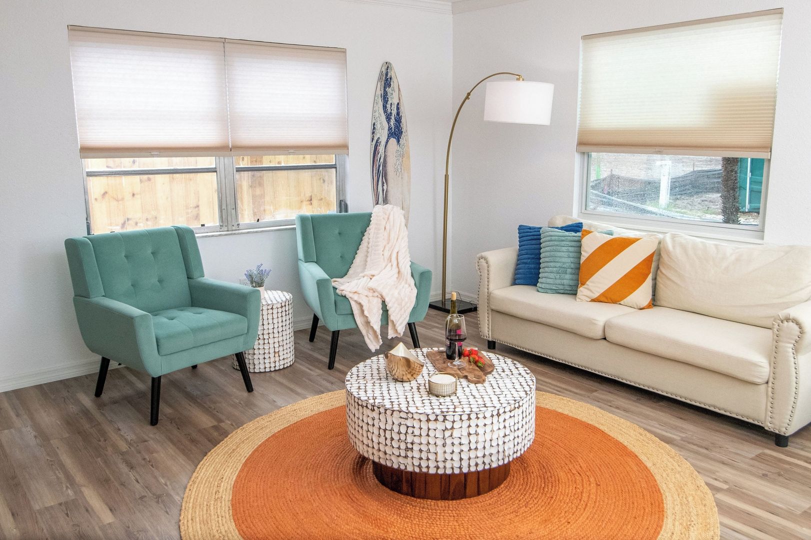 A living room with teal armchairs, a white sofa with colorful cushions, a round coffee table, and a floor lamp.