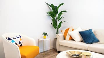 Een woonkamer met een gele fauteuil, een witte bank, een ronde salontafel en een potplant.