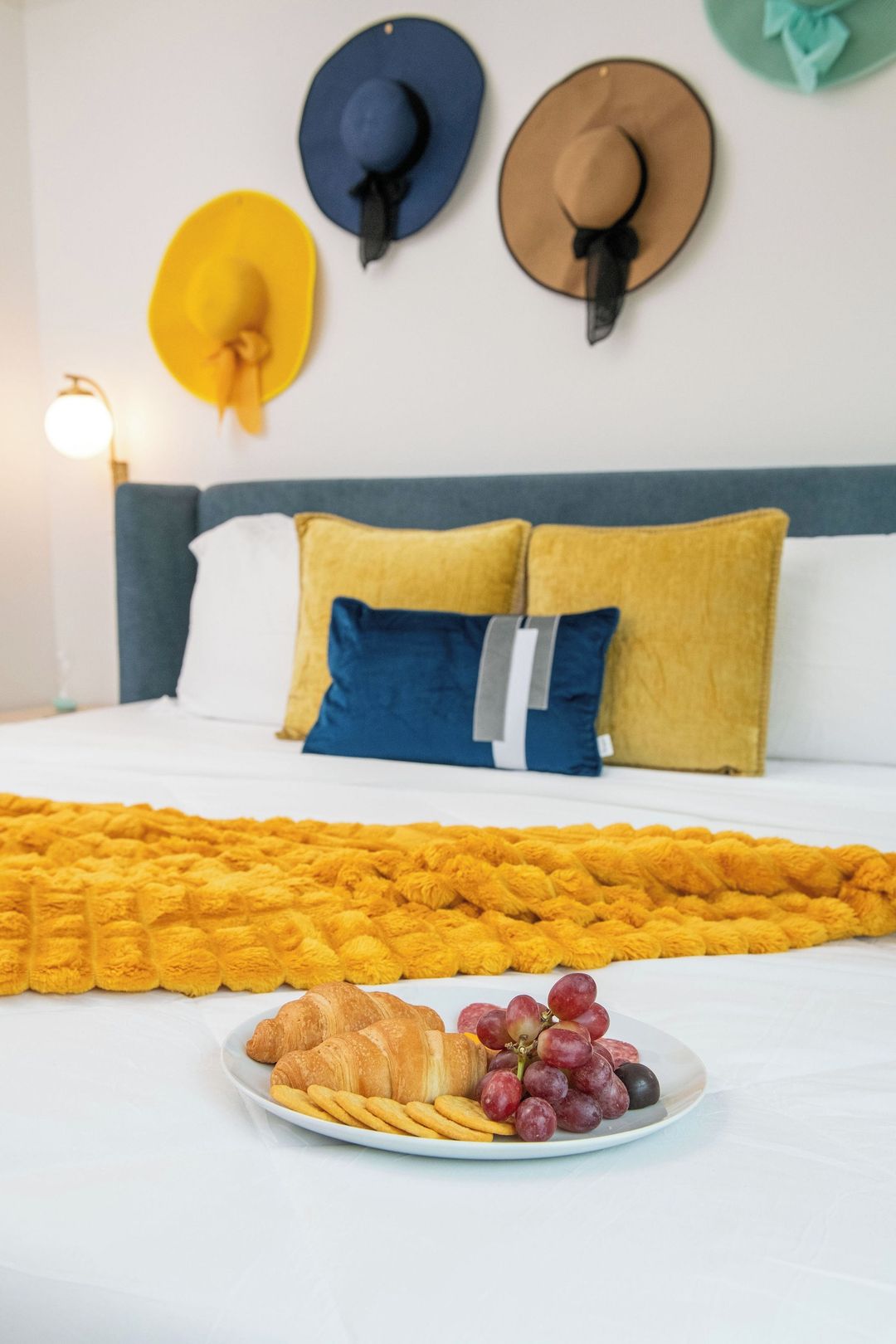 Ein ordentlich bezogenes Bett mit einer gelben Decke, ein Tablett mit Croissants, Trauben und Keksen.