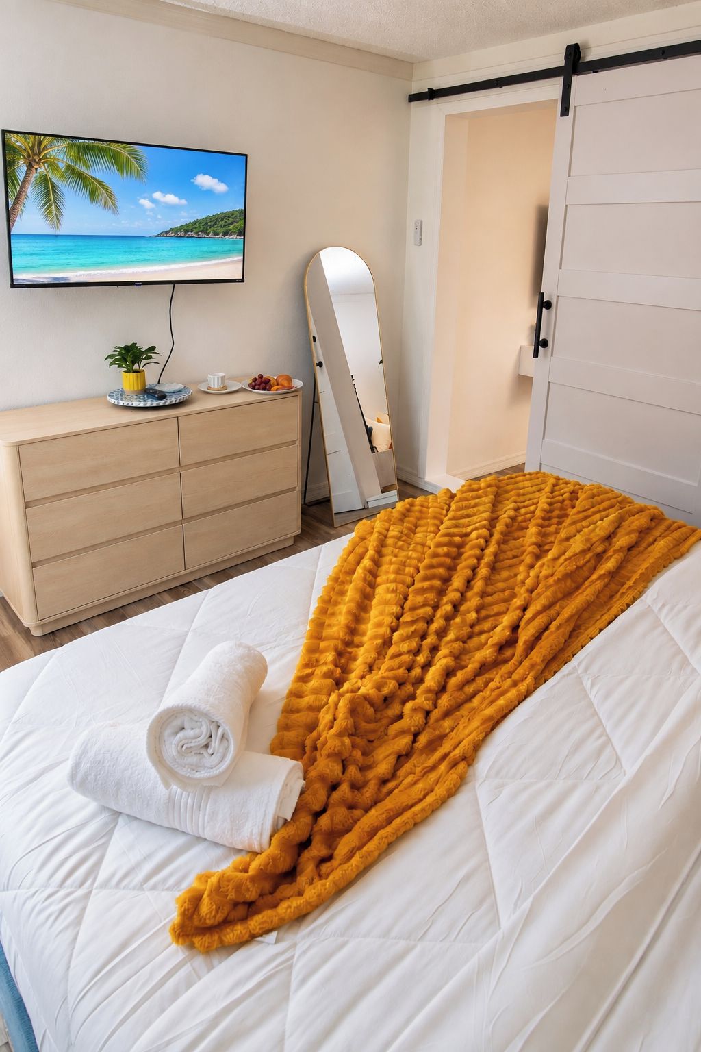 Un dormitorio con cama, televisor, cómoda, espejo y puerta corredera.