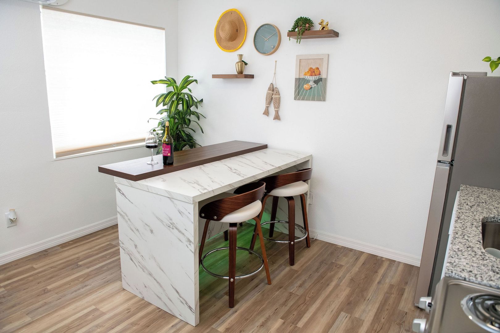 Una cocina con encimera de mármol, dos taburetes de bar, un refrigerador y una planta en maceta.