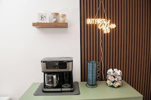 Une machine à café posée sur une table, un panneau lumineux au néon et un porte-tasses.