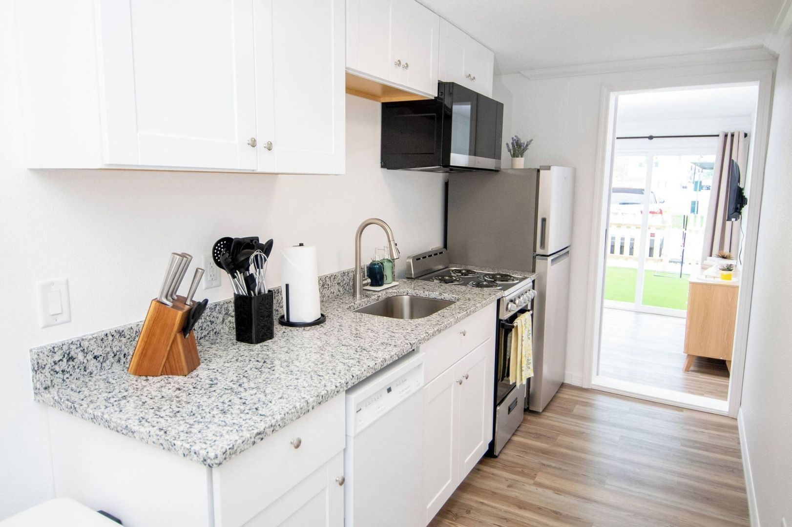 A compact kitchen with white cabinets, a granite countertop, a stainless steel stove, and a built-in microwave.