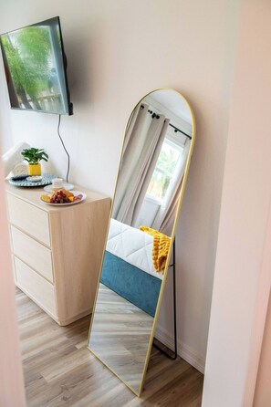 Ein Schlafzimmer mit einem Bett, einem Nachttisch mit Pflanze und einem Spiegel.