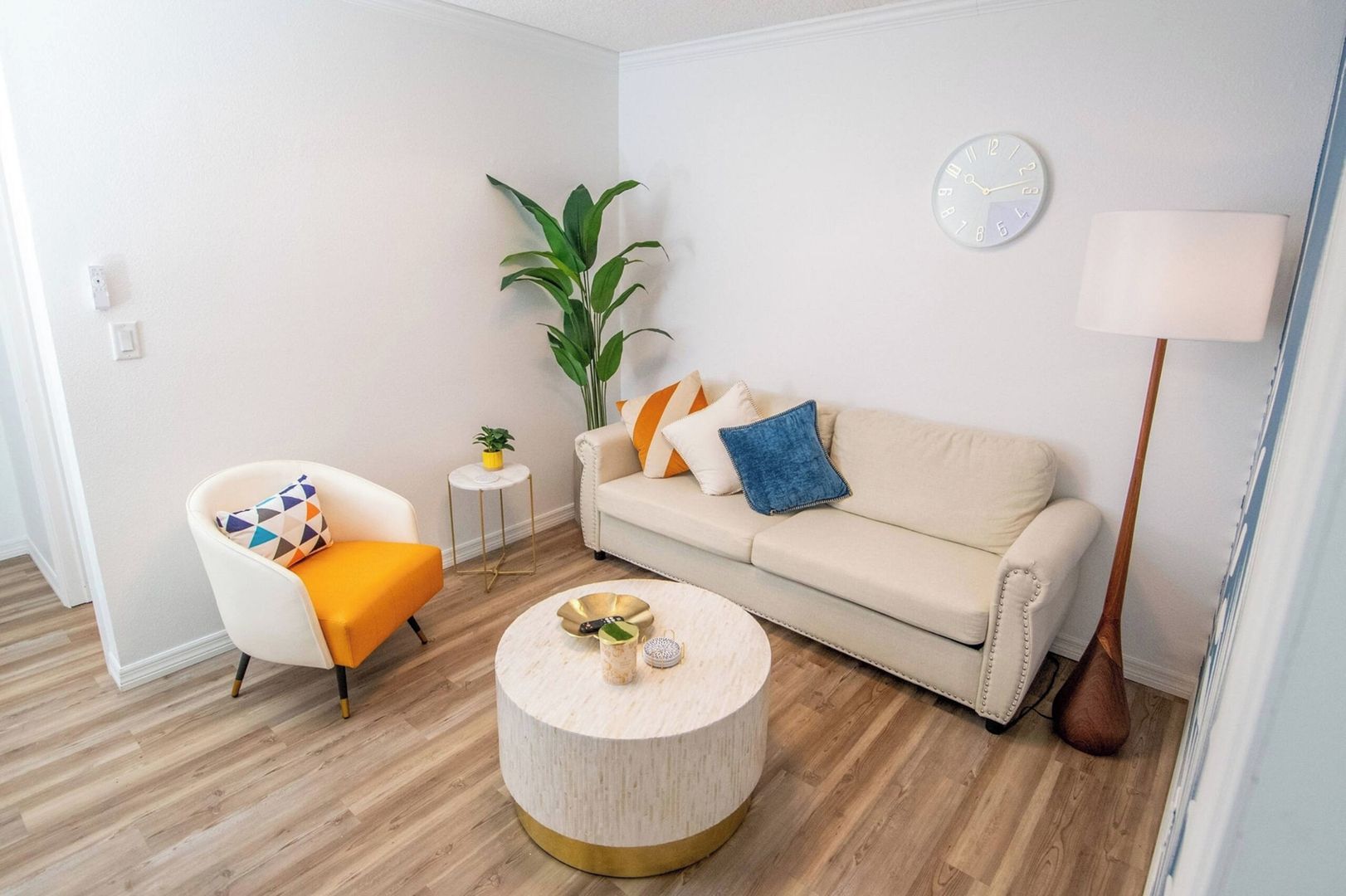 Un salon moderne avec un canapé, un fauteuil, une table basse ronde et une plante en pot.