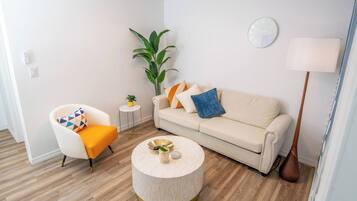 Un salon moderne avec un canapé, un fauteuil, une table basse ronde et une plante en pot.