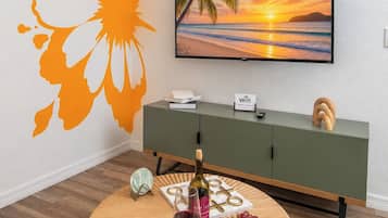 A room with a round wooden coffee table, a television on the wall, a green cabinet, and a wall decal of a sun and flower.