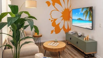 A modern living room with a sofa, a round coffee table, a potted plant, a TV, and a decorative wall mural.