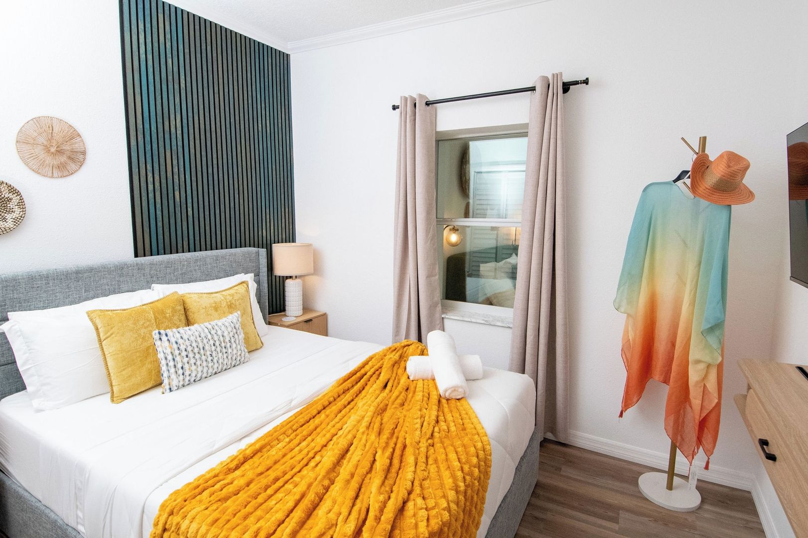 Ein Hotelzimmer mit einem Bett, einem Vorhangfenster, einer Lampe und einem an der Wand montierten Fernseher.