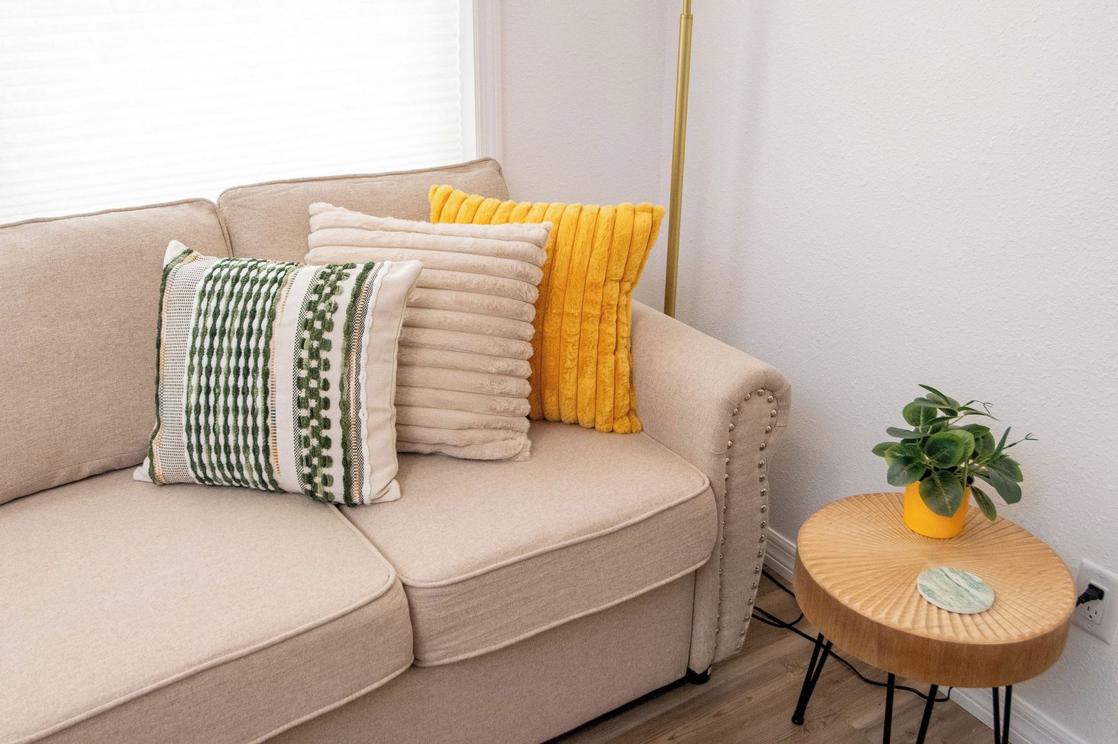 A beige sofa with multiple cushions, a small wooden side table with a plant, and a tall floor lamp.