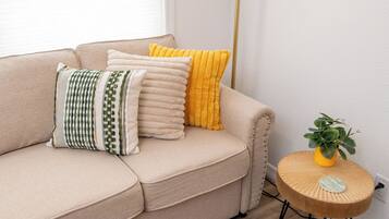 A beige sofa with multiple cushions, a small wooden side table with a plant, and a tall floor lamp.