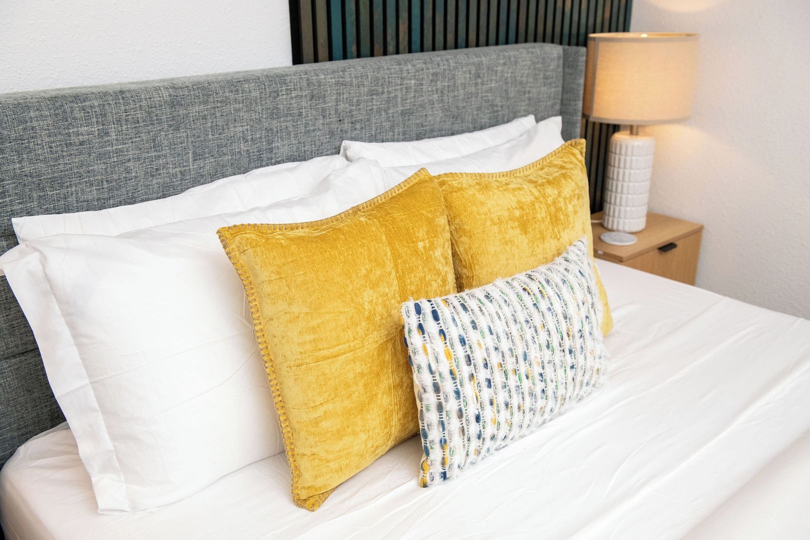 A bed with white bedding, a grey headboard, and two pillows, one yellow and one multicolored.