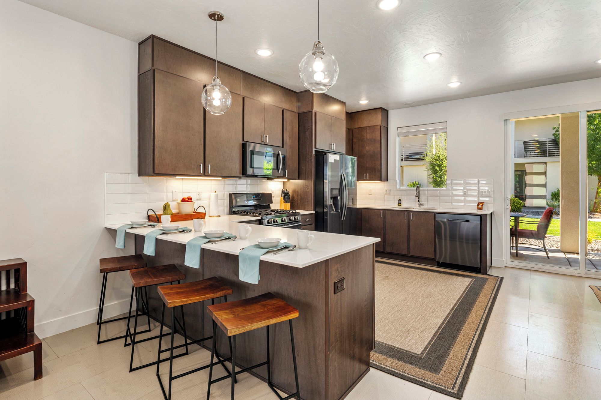 A modern kitchen with dark wood cabinets, a central island with stools, stainless steel appliances, and pendant lighting.