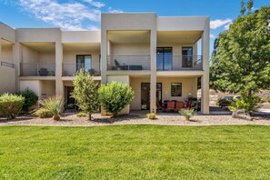 Ein mehrgeschossiges Wohngebäude mit Balkonen, einer Terrassenanlage mit Gartenmöbeln und einem gepflegten Rasen.