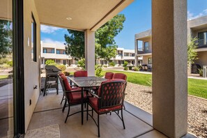 Eine Terrasse im Freien mit Tisch, Stühlen, einem Grill und Blick auf einen Gebäudekomplex.