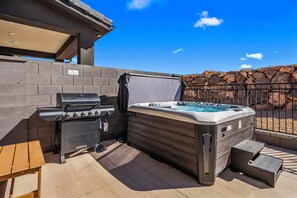 Un patio exterior con una parrilla, un jacuzzi y un muro de piedra.