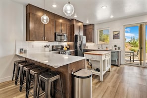 A modern kitchen with a central island, stainless steel appliances, and bar stools. - Lofts 45, PS5, Balcony Views, and Resort Amenities! (Saint George)