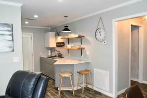 Une cuisine compacte dotée d’un îlot central, de tabourets en bois, d’un luminaire suspendu et d’une horloge murale.