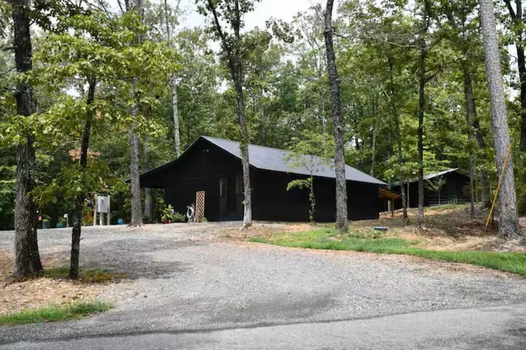 A rustic cabin with a gravel driveway, surrounded by trees.