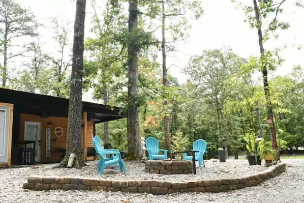 A covered outdoor seating area with four blue chairs and a stone fire pit, surrounded by a stone border.