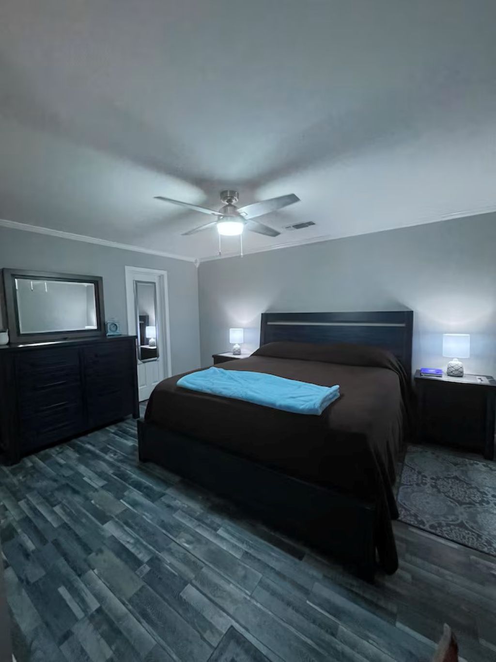 A bedroom with a bed, a ceiling fan, a dresser, and a nightstand with a lamp.