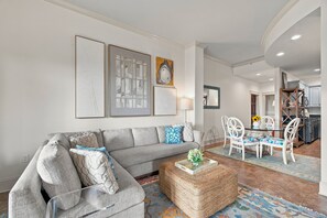 A living room with a grey sofa, a coffee table, and a dining area with white chairs. - Sea Gate #102, This 1 bedroom suite on St. Simons (St. Simons Island)