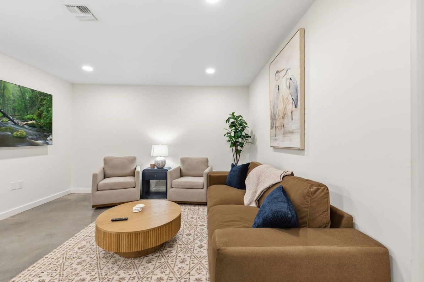A modern living room with a sofa, armchairs, a coffee table, and a painting on the wall.