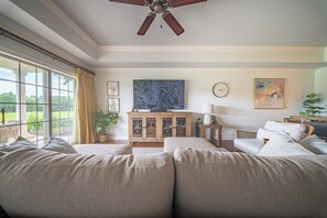 A living room with a large window, a ceiling fan, a television, and a clock on the wall. - The Centre at Reunion-1356 (Kissimmee)