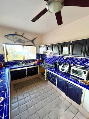 A kitchen with blue tiles, a ceiling fan, and a window with a view of palm trees. - Best Ocean View and Pool (San José del Cabo)