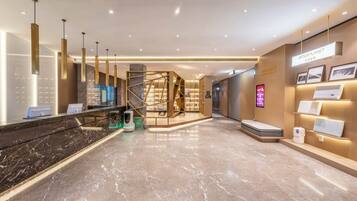 Un moderno vestíbulo de hotel con mostrador de recepción, quiosco informativo digital y una escalera que conduce a los pisos superiores.