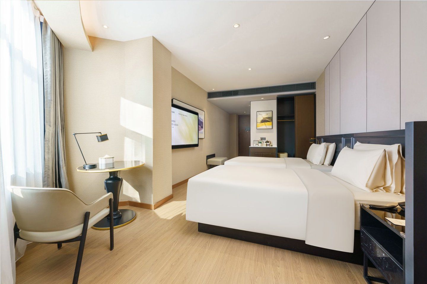 A modern hotel room with a large bed, a desk with a chair, a flat-screen TV, and a wardrobe.