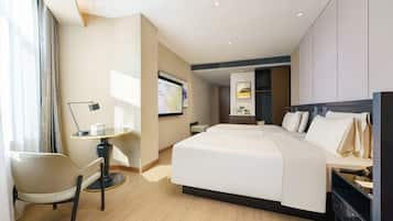 A modern hotel room with a large bed, a desk with a chair, a flat-screen TV, and a wardrobe.