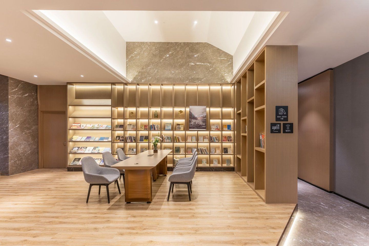 A modern library with a wooden table and chairs, bookshelves, and a marble wall.