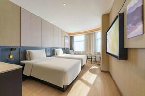 Habitación de hotel con dos camas, un escritorio, una silla, un televisor y una ventana con cortinas.