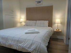 A neatly made bed with a checkered duvet, two bedside lamps, and a headboard with vertical slats. - Nice cozy Bedroom with ensuite bathroom in Downtown Cooksville, Mississauga (Mississauga)