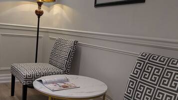 A room with a round table, two patterned chairs, a floor lamp, and a framed picture on the wall.