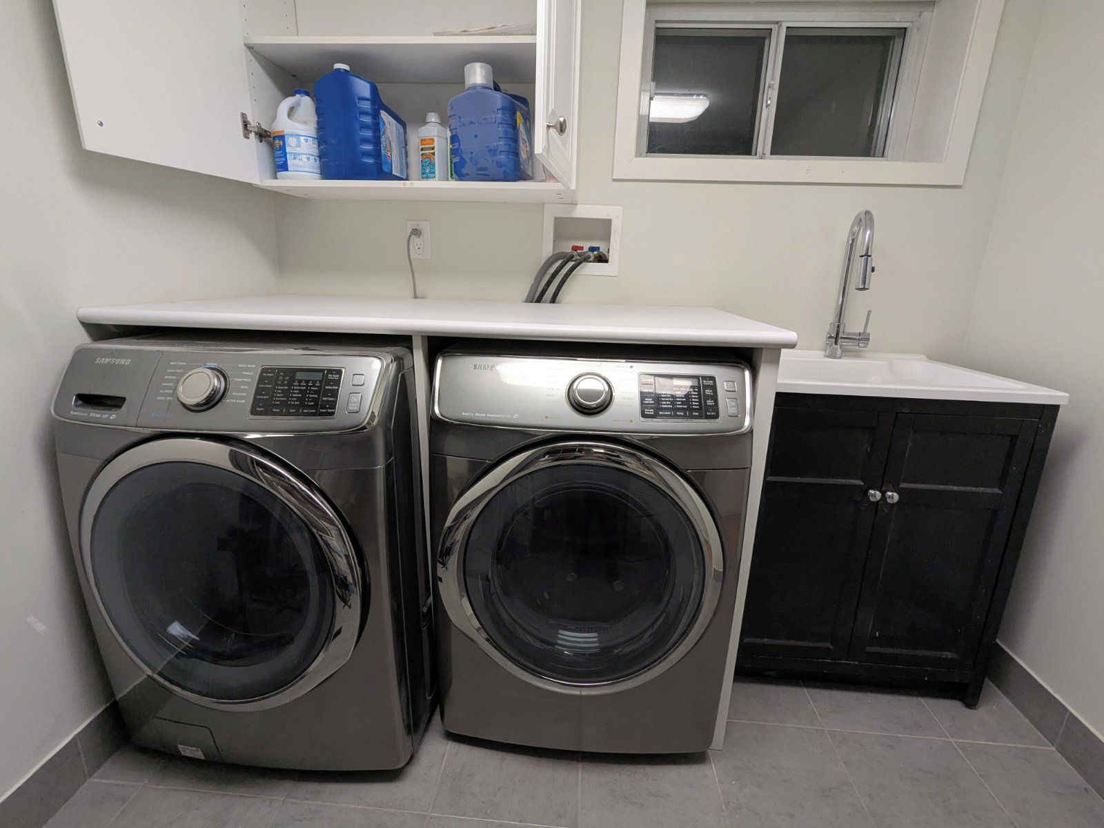 A laundry area with two front-loading washing machines, a sink, and a cabinet.