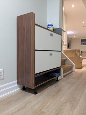 Ein kompakter, multifunktionaler Stauraum mit Holzoptik und weißem Unterteil, platziert in einer Diele mit Treppe, auf welcher eine Waschmittelschachtel steht.