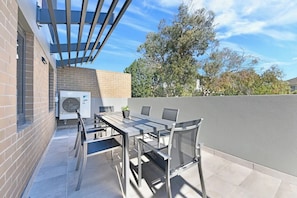 An outdoor patio with a table and chairs, a pergola, and a brick wall. - Modern Fully Furnished Studio Kingsford (Kingsford)