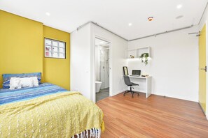 A bedroom with a bed, a desk, and a bathroom visible through an open door. - Modern Fully Furnished Studio Kingsford (Kingsford)